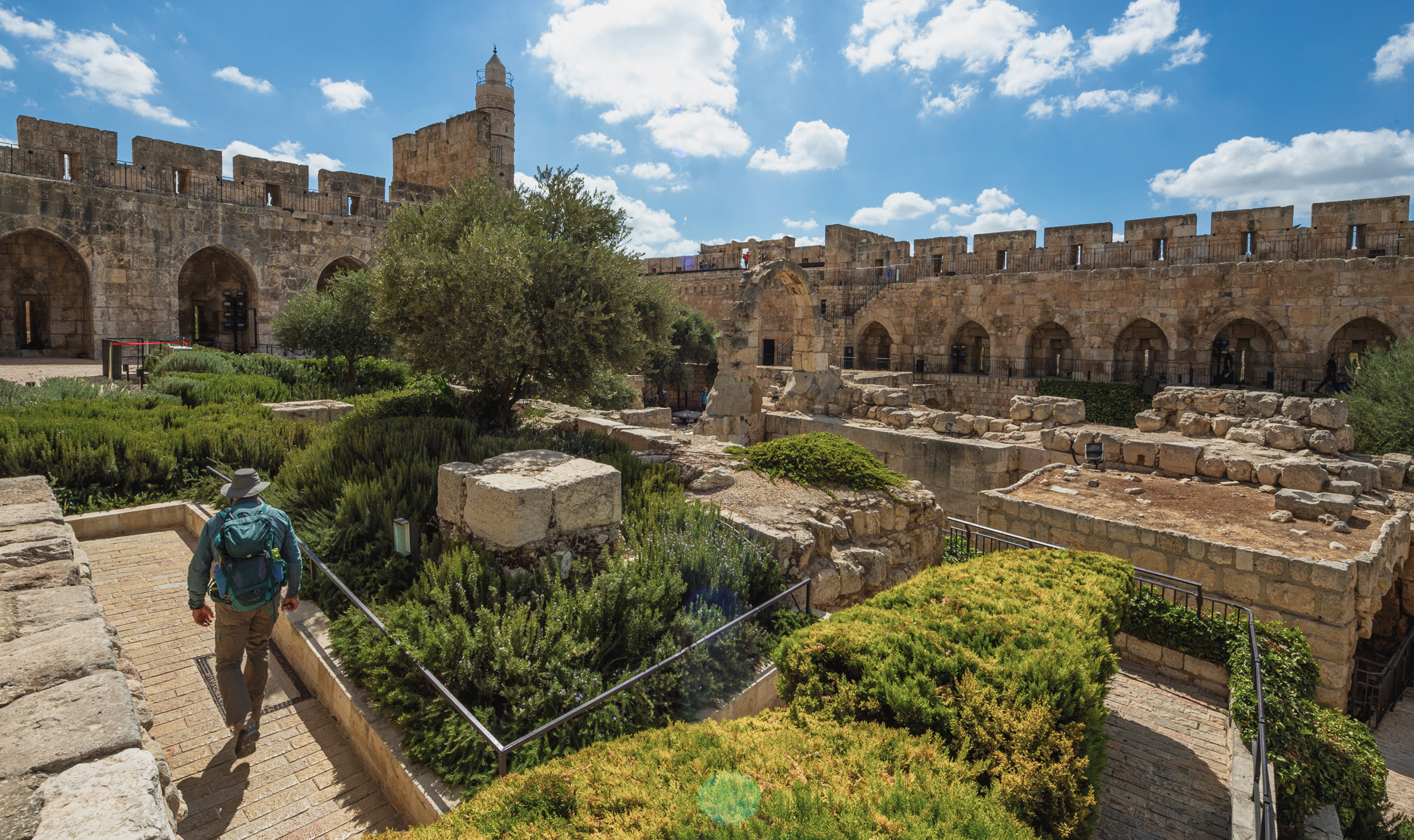 Tourist explores ancient stone fortress, lush greenery surrounds.