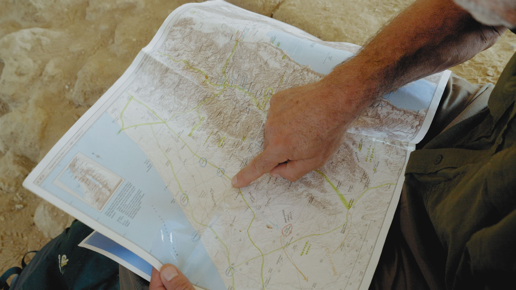 Person pointing at map in desert.