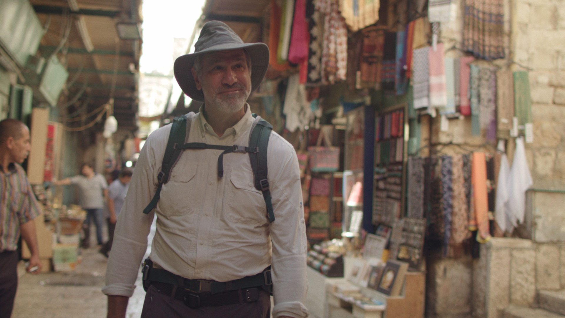Man walking through market with backpack and hat.